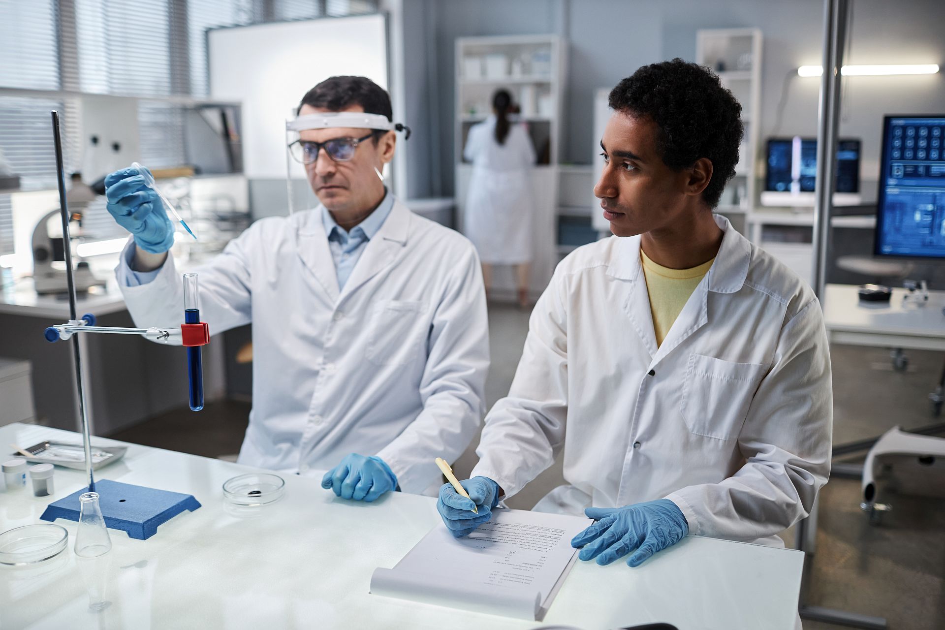 Portrait of young intern in scientific laboratory watching male scientist at work