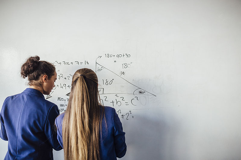 two school girls in front of a white board working on some mathematical equations