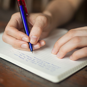 A person writing in a book with a blue pen