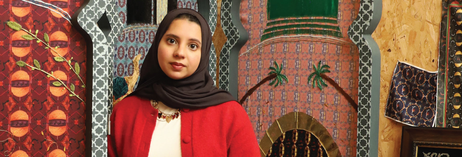 Artist Farwa Moledina poses in front a several mounted colourful textiles.