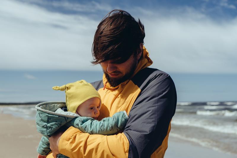 A father cradles his young baby on a windswept beach