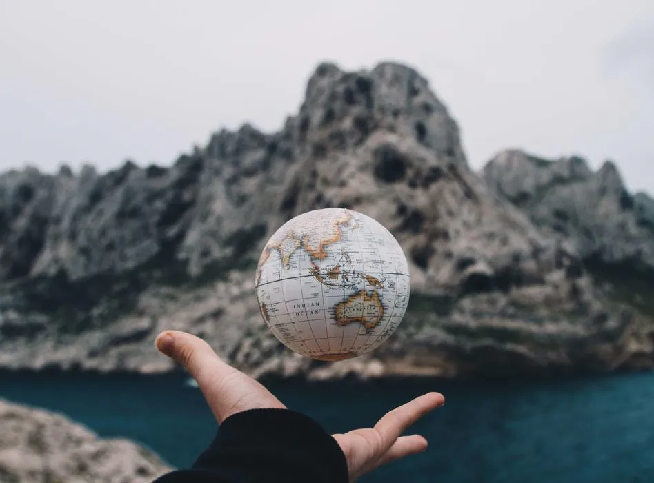 globe with a hand underneath and mountains in the background