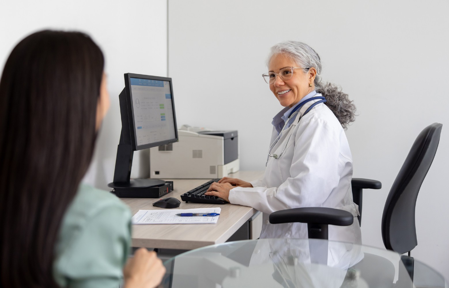 A GP takes notes on her computer while meeting with a patient