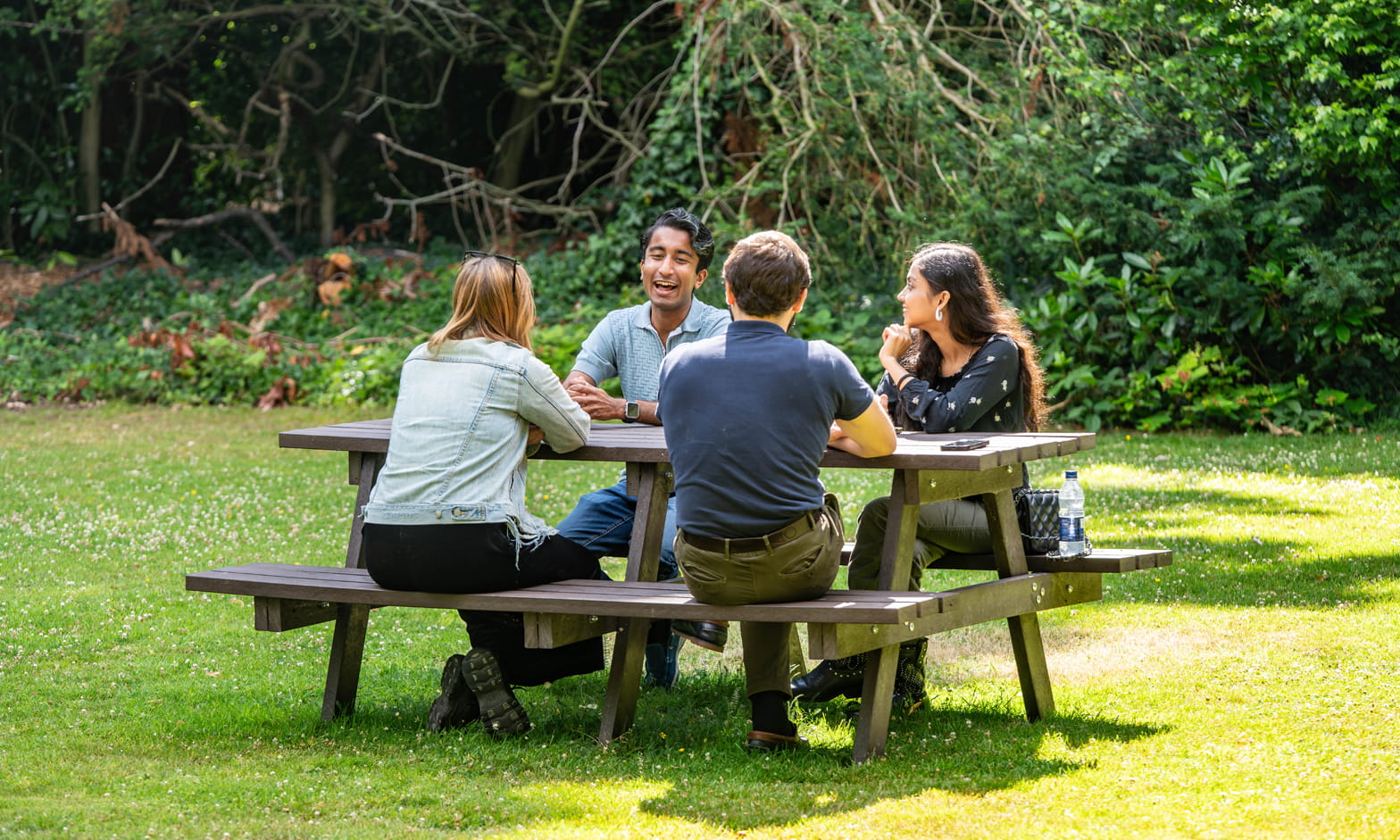 Four students sitting at a picnic table in a leafy, green park space