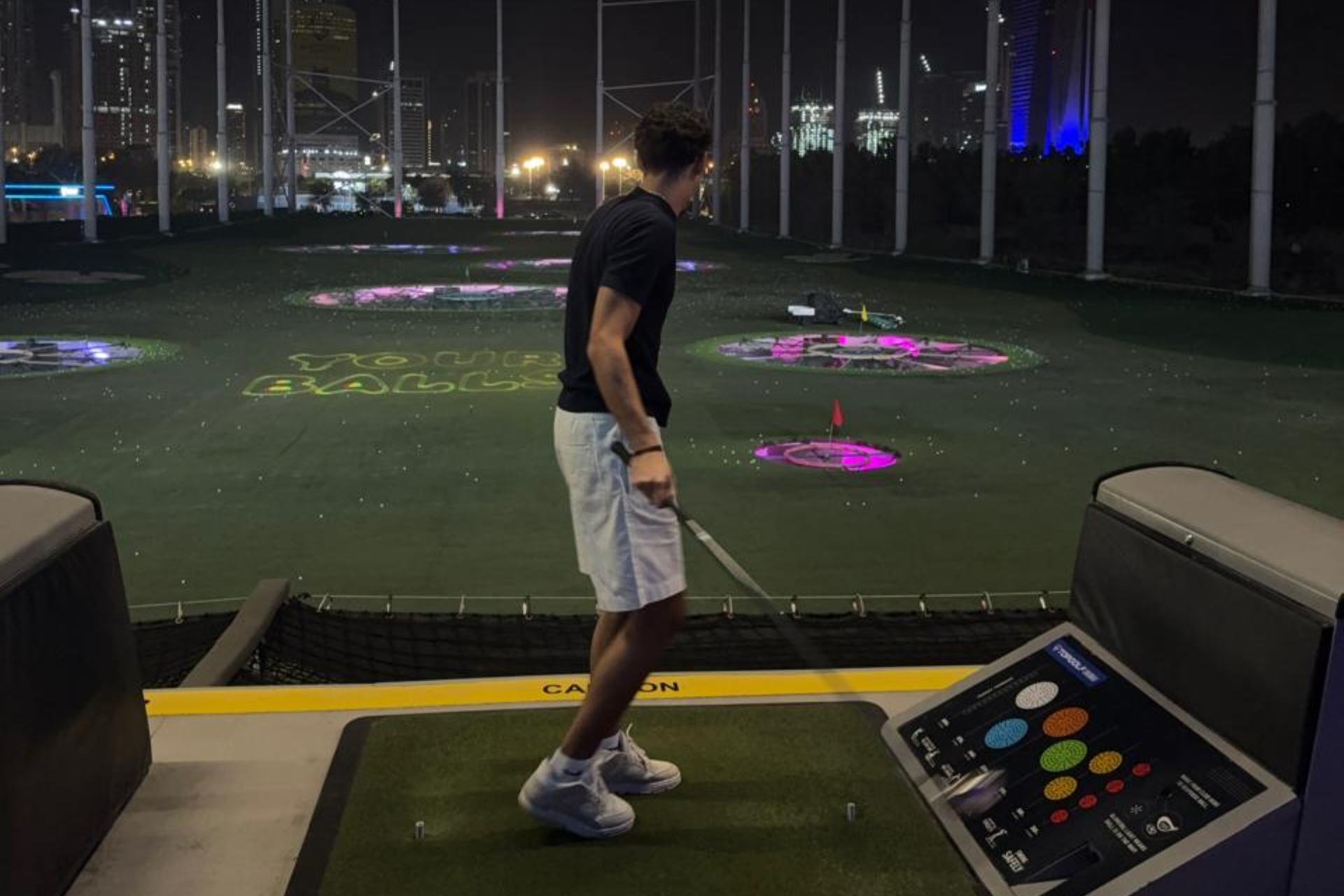 Playing golf at Topgolf Dubai driving range at night.