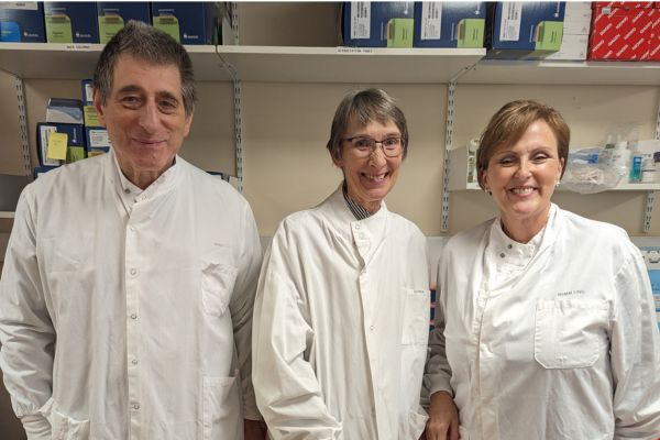 Three scientists in white lab coats smiling at the camera in an office.