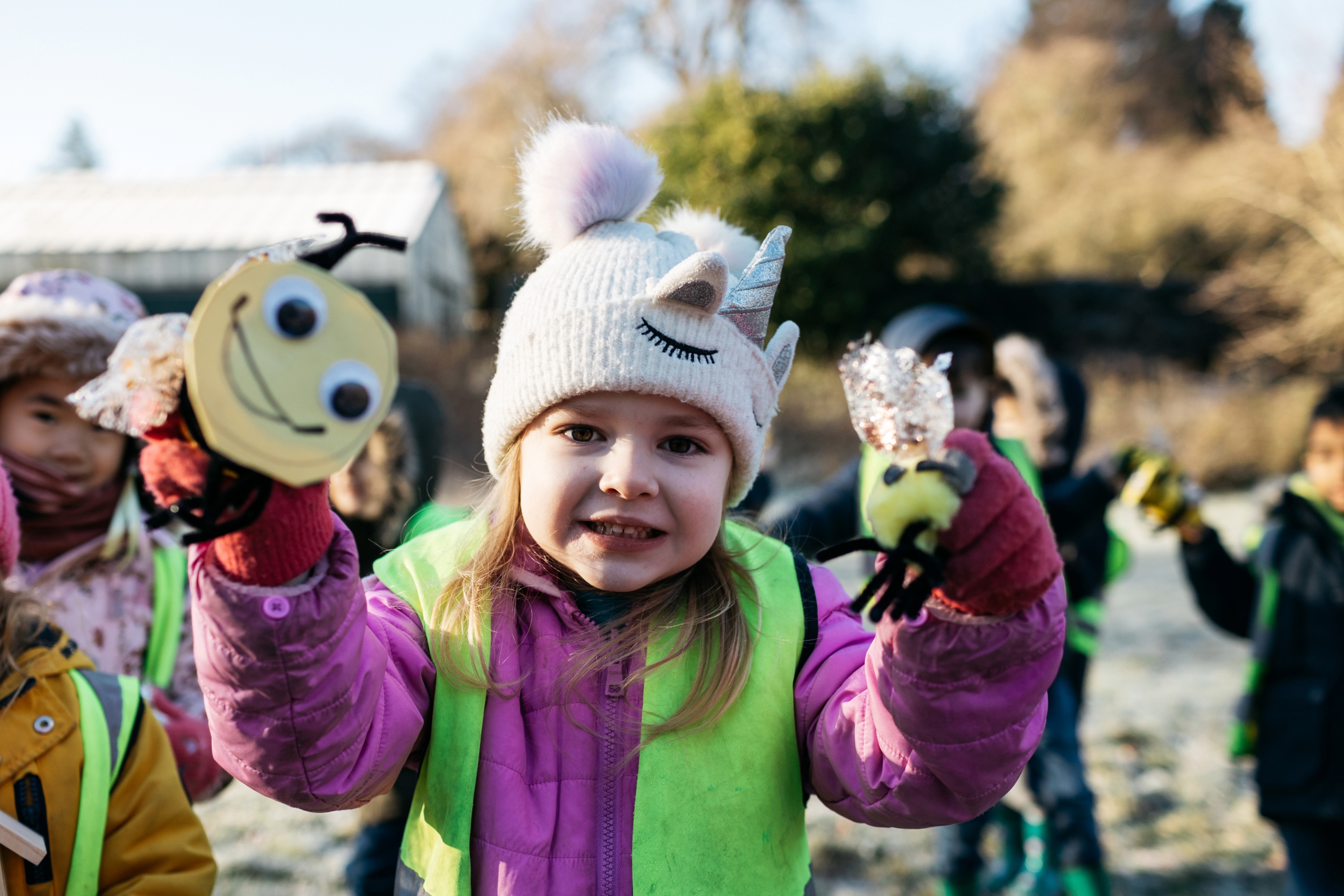 A young girl in winter clothing holding up toys