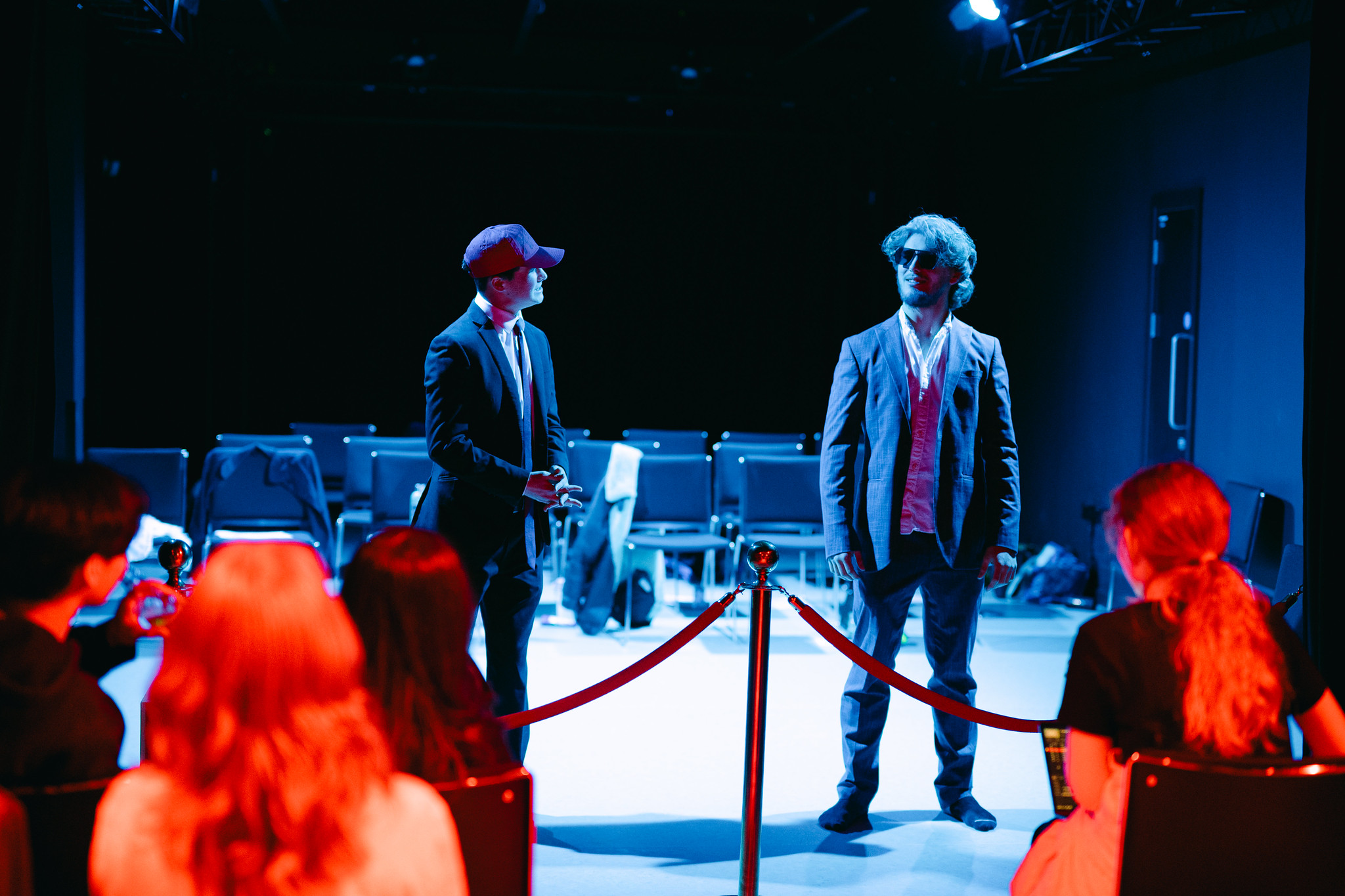 Two students stand on a stage performing with the audience in the foreground watching.