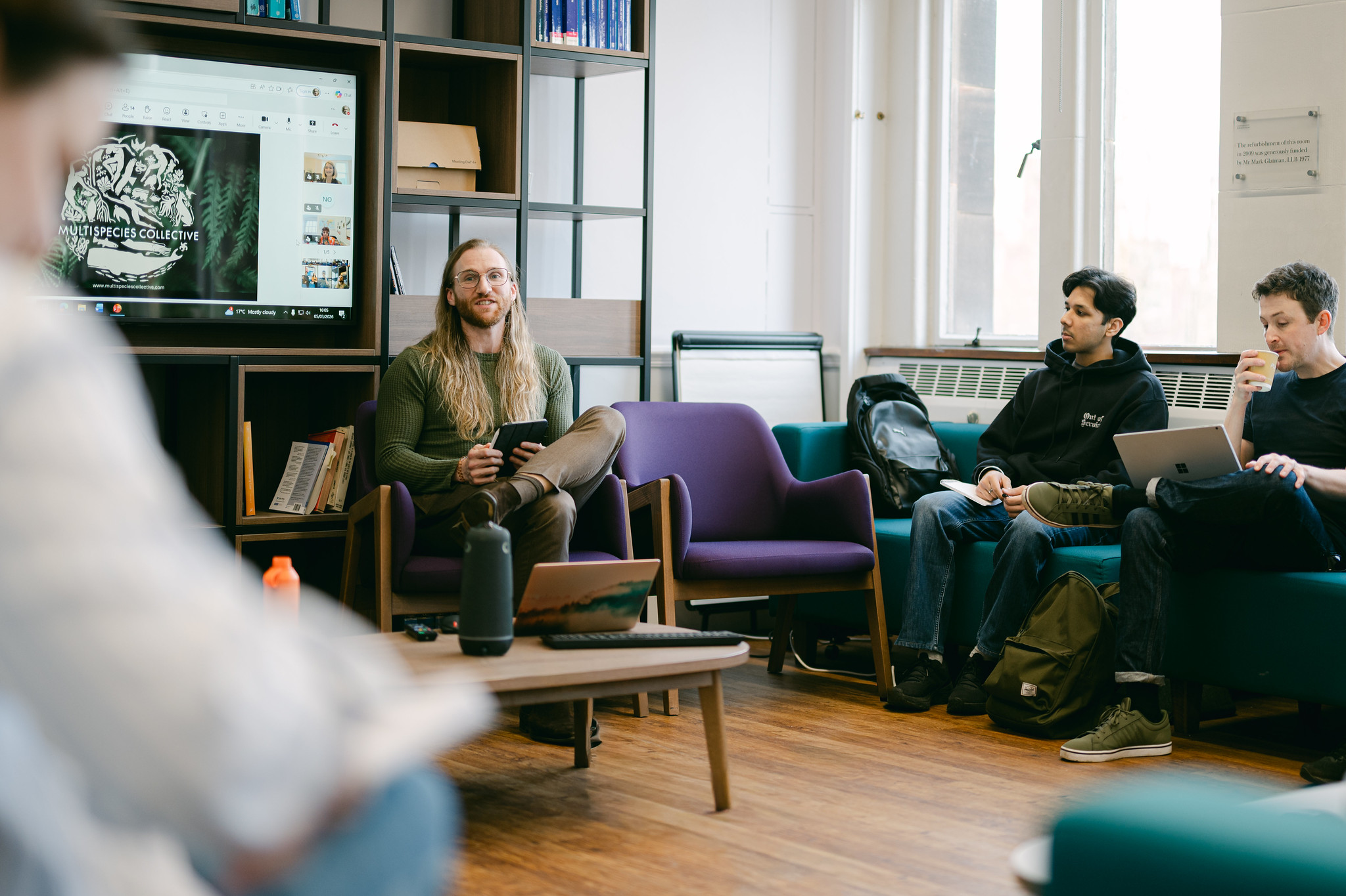 Dr Iyan Offor talks to members of the Multispecies Collective. Behind him is a television with the Collective's logo on. 