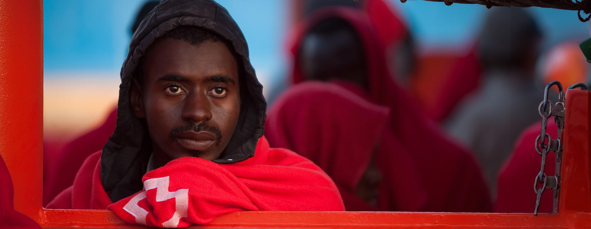 An African migrant wrapped in an orange blanket staring out into the middle distance