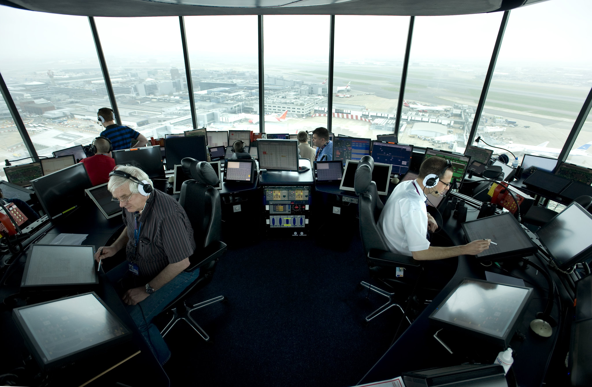 Air traffic controllers sat in control tower at Heathrow Airport in London, UK with airport and planes in the background