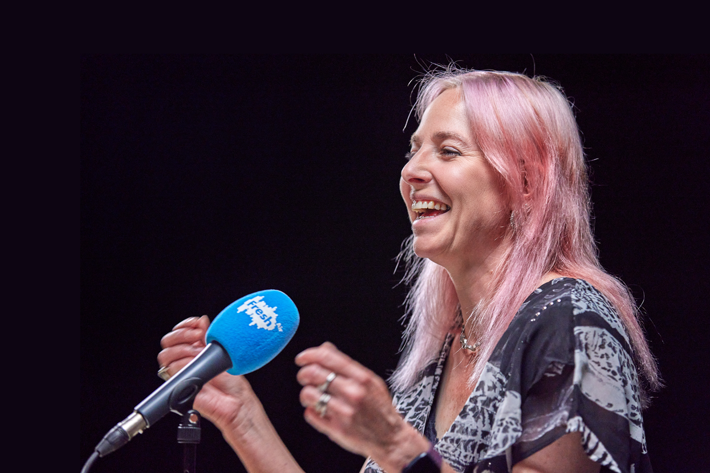 Professor Alice Roberts laughing with a microphone in front of her