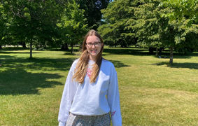 Liberal Arts and Natural Sciences student Alice stands on the grass in front of some beautiful green trees