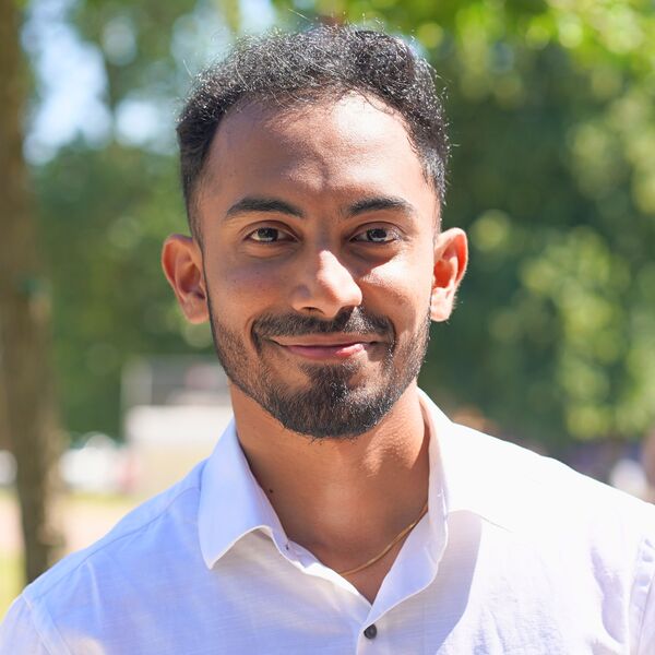 Amruth smiling towards the camera over a background of green trees on campus