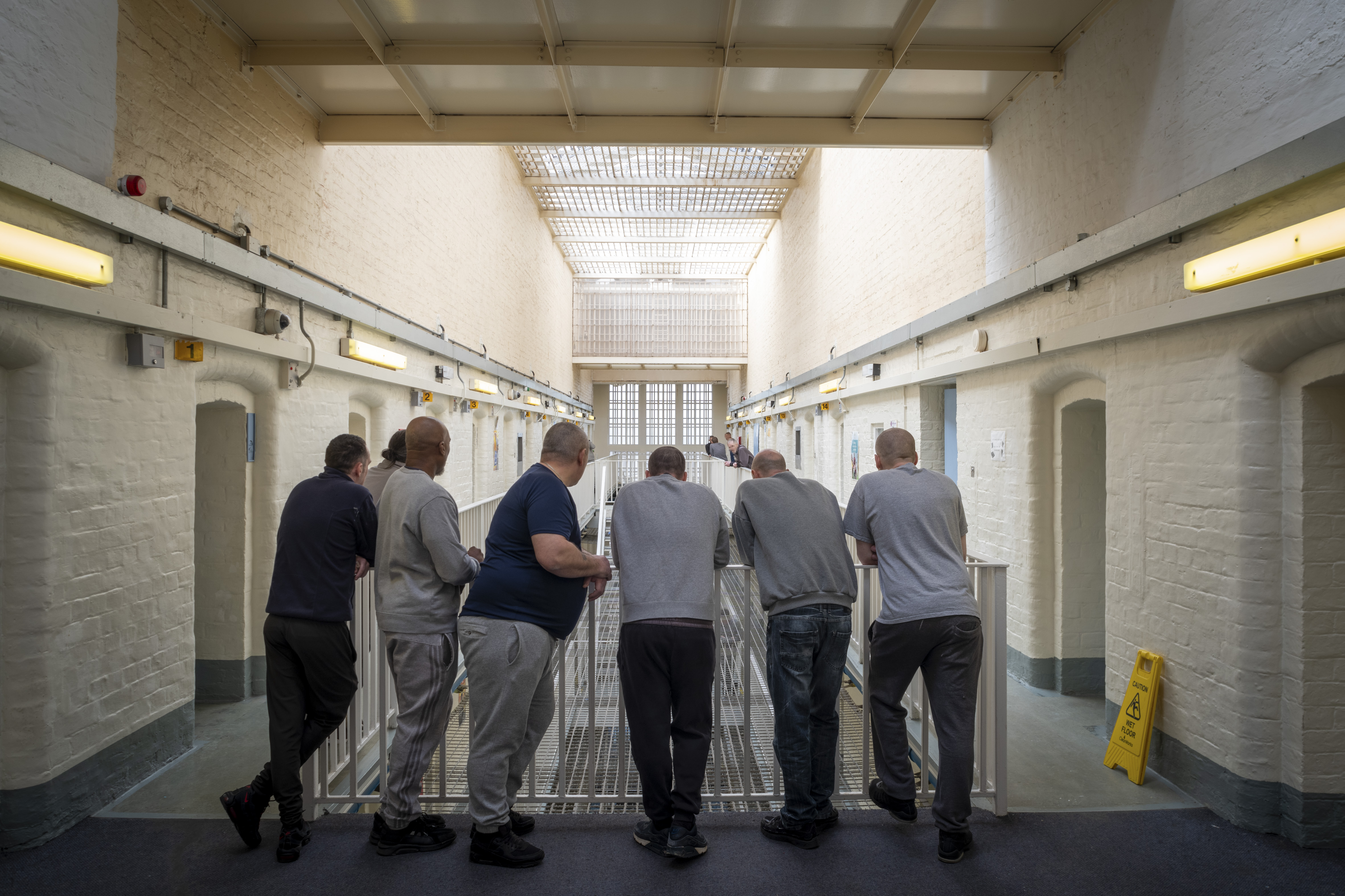 A group of prisoners gathered on a landing area in a prison looking over a railing to the floor below