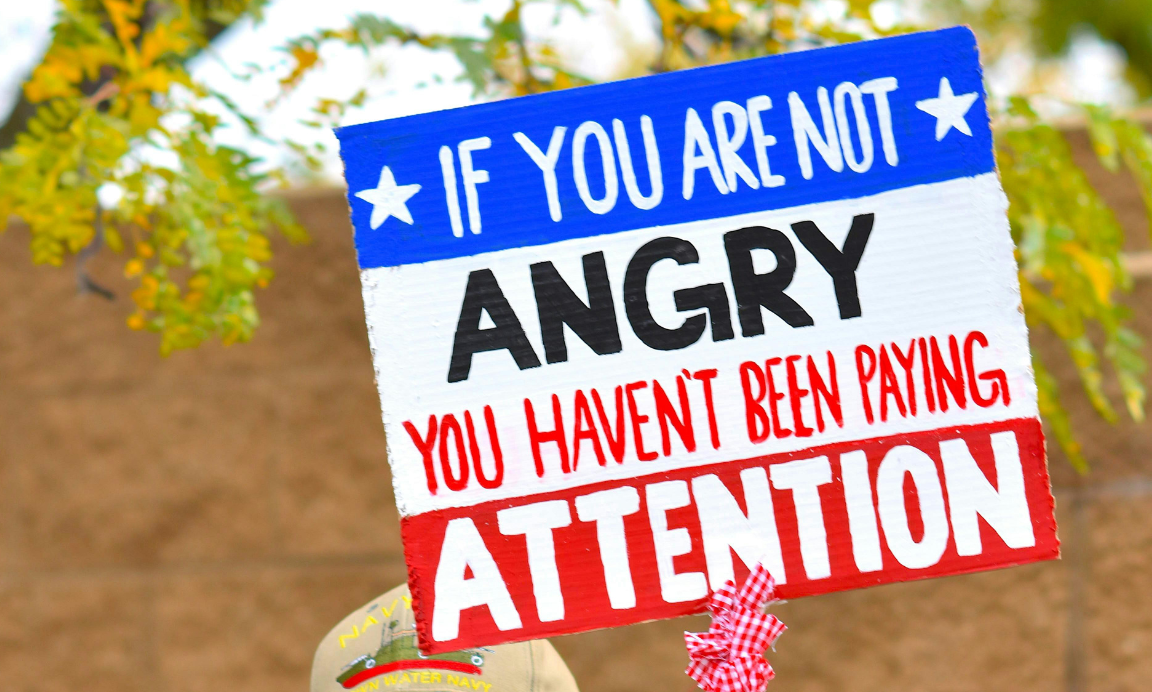 A protest sign saying: if you are not angry you haven't been paying attention.