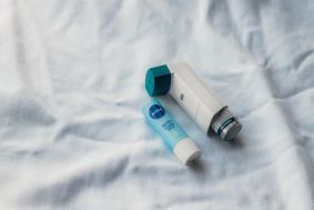 An inhaler and lotion stick on a white hospital sheet