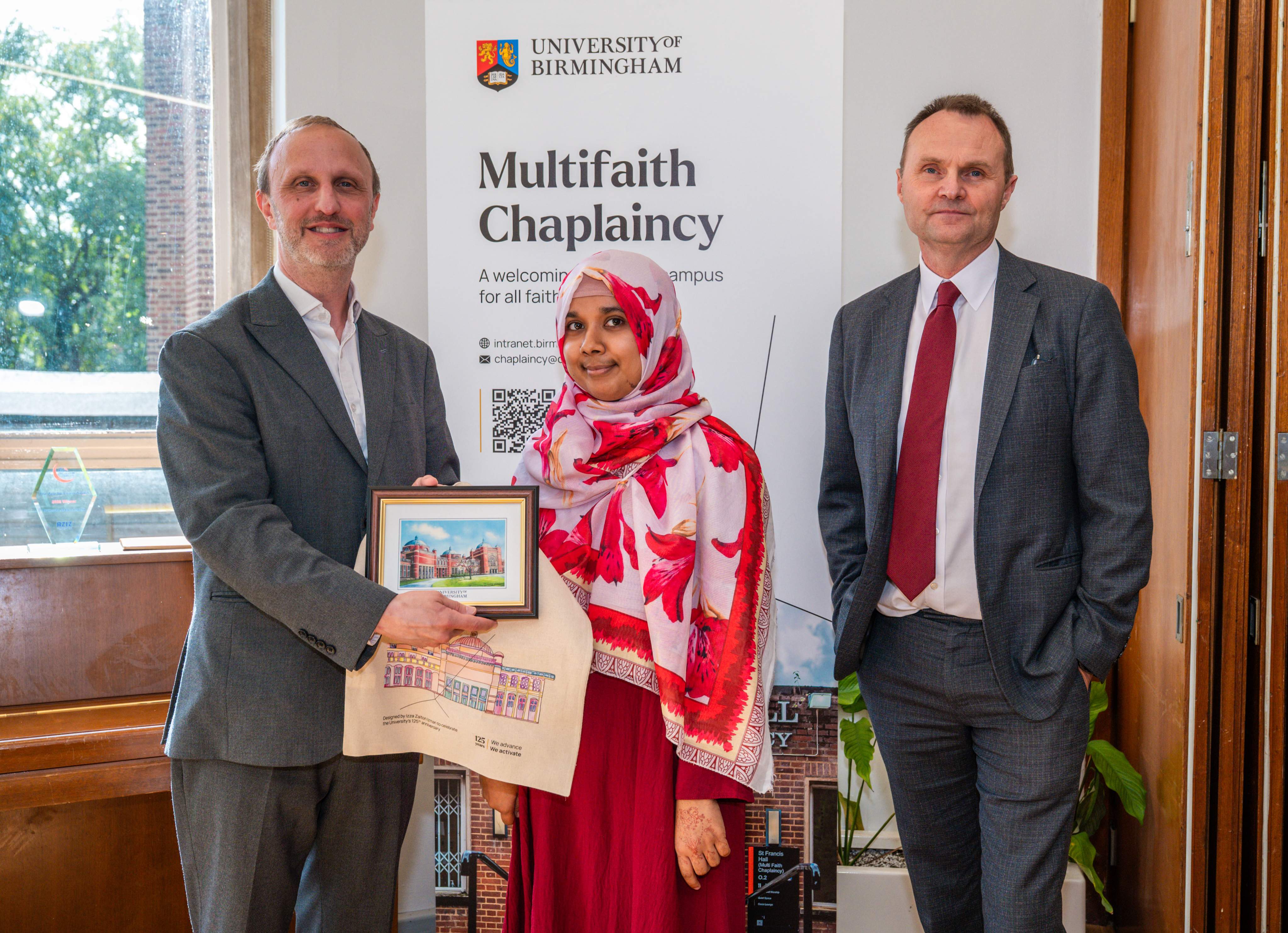 Three people stand together, in front of a sign that reads 'multifaith chaplaincy'