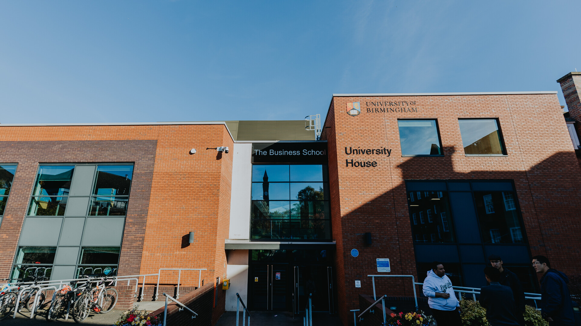 Exterior of Birmingham Business School building with a group of three students stood outside talking.