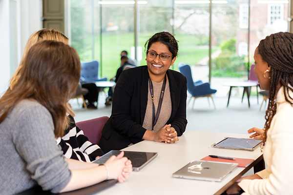 A female member of staff and three students sitting at a white table talking and smiling.