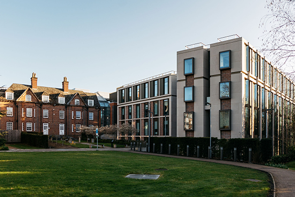 Modern and historic university buildings side by side with a green lawn and pathways in the foreground.