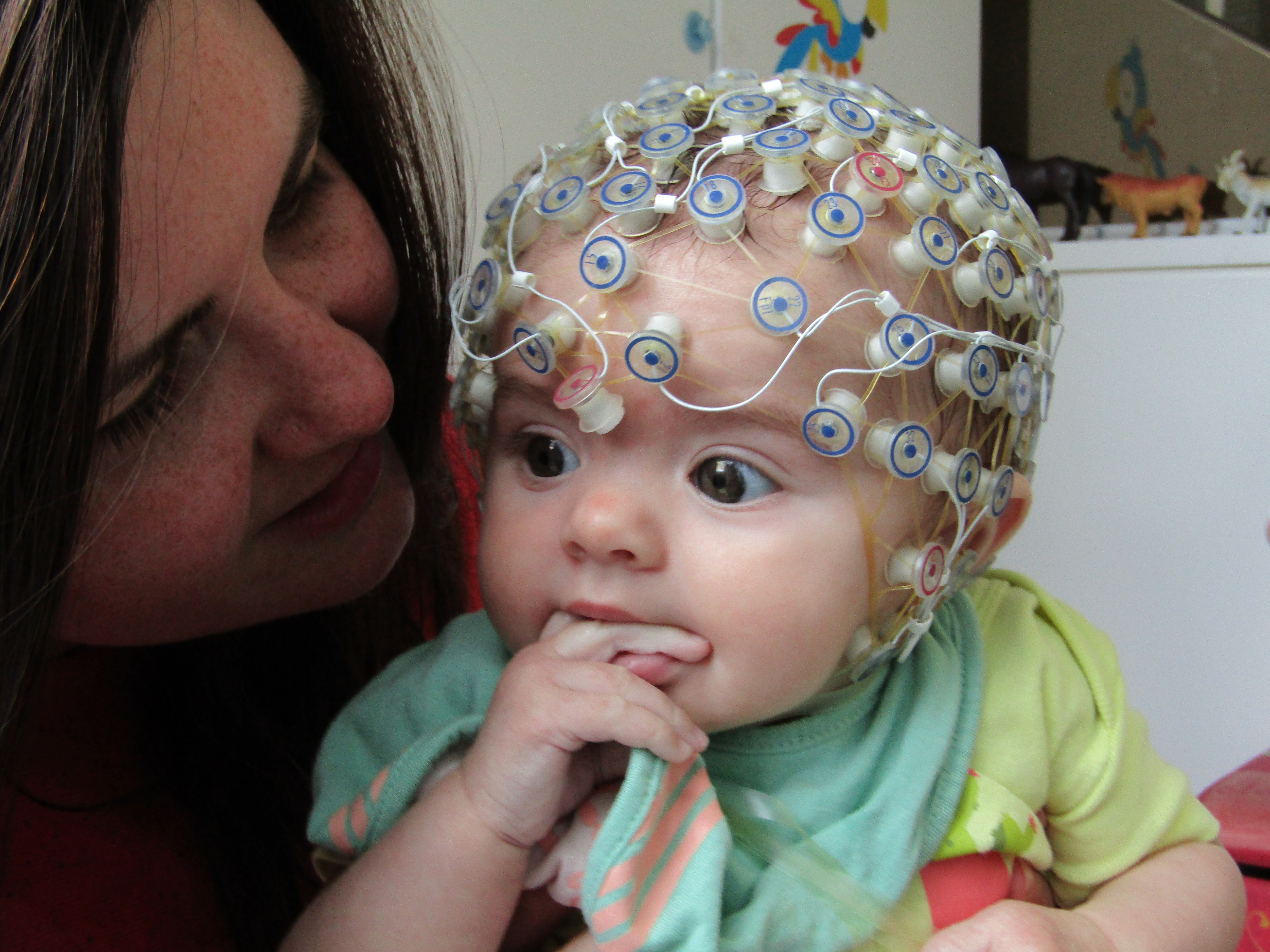 Baby with an EEG cap on to take part in the study, being held by their parent
