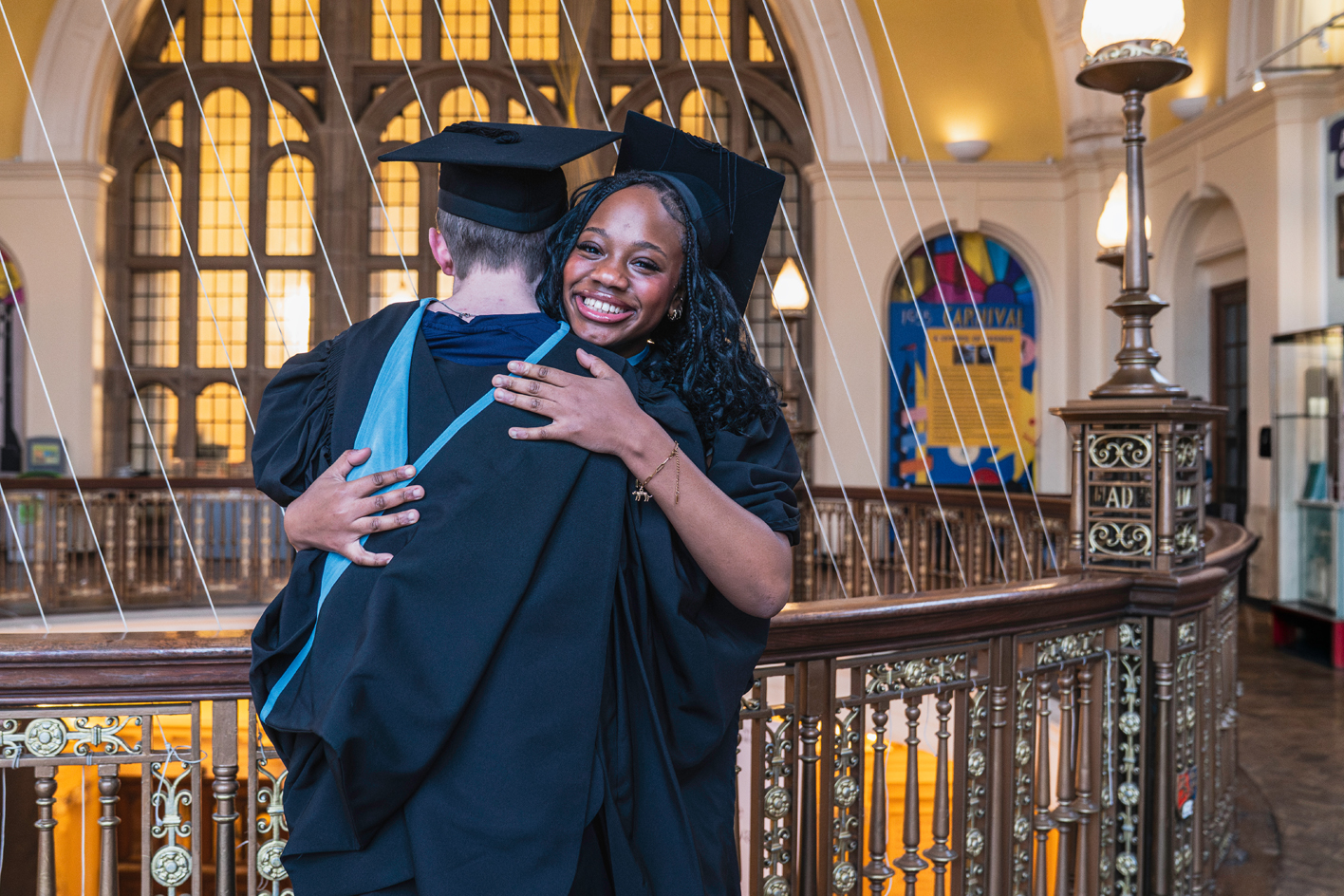 Two students in graduation gowns and mortarboards hugging each other in Aston Webb's whispering gallery