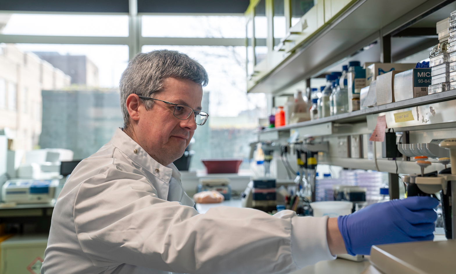 A researcher in a white lab coat and blue Latex gloves working in a lab setting