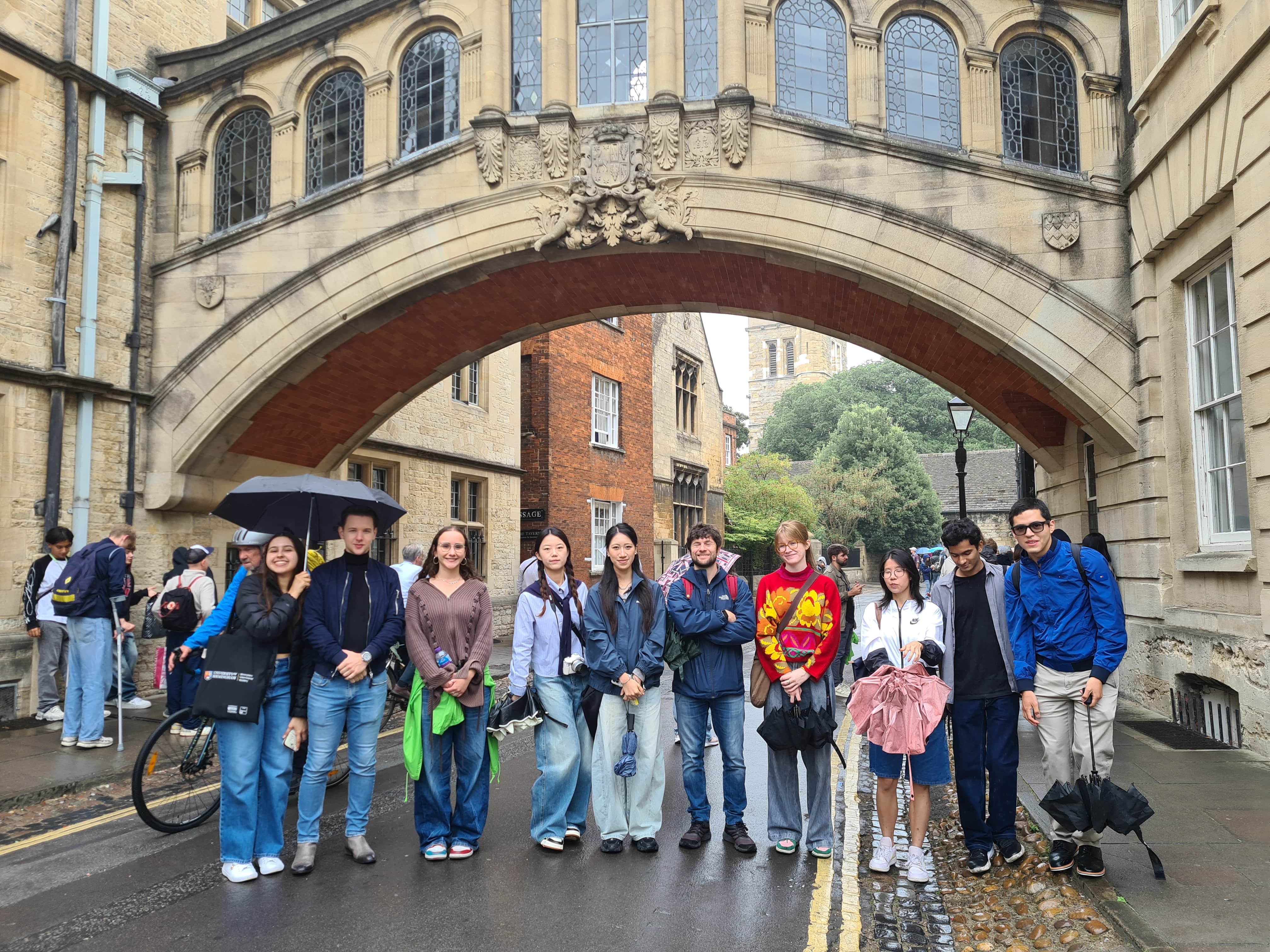 Summer school students posing in the streets of Oxford holding umbrellas