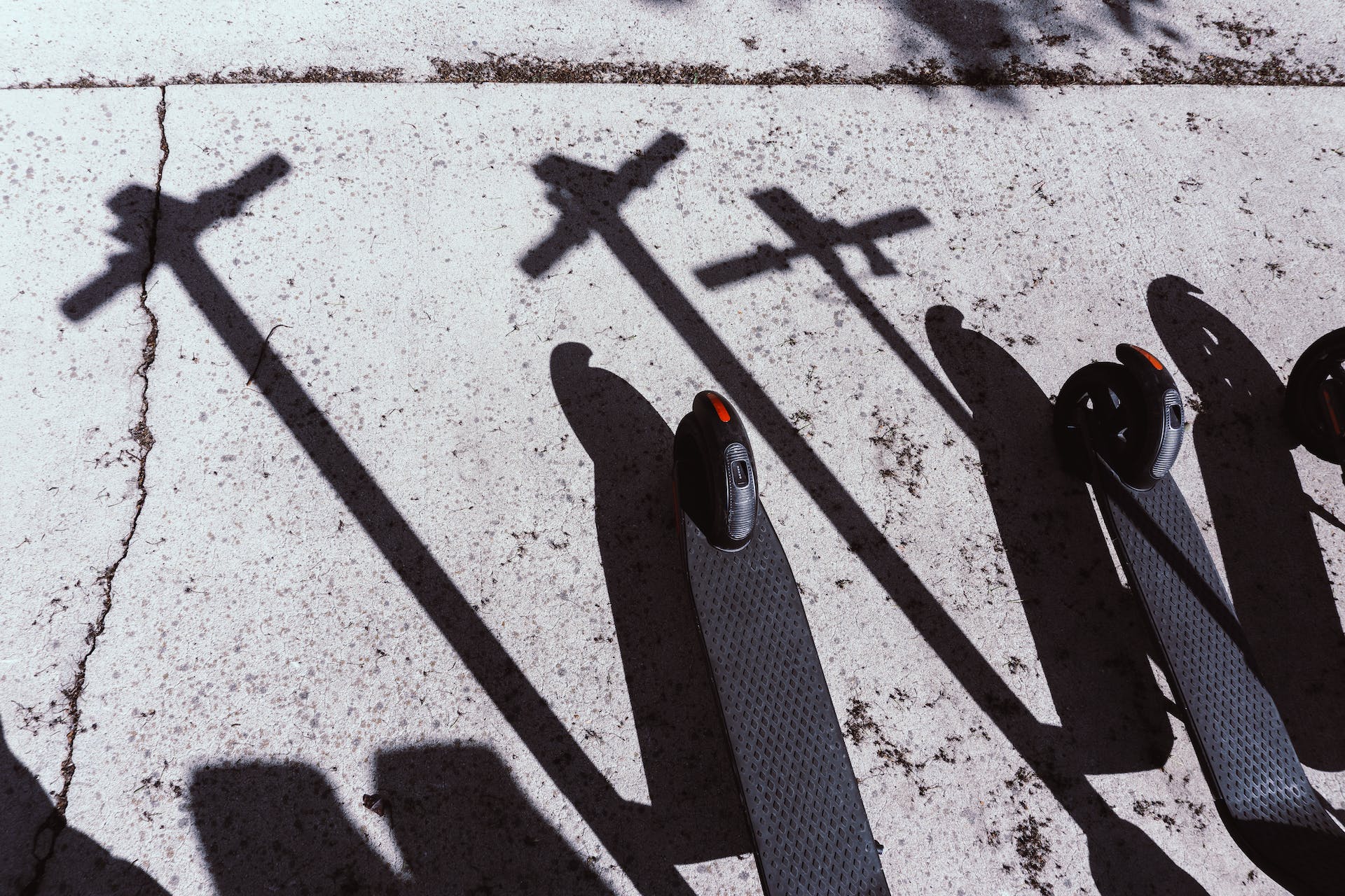 Black e-scooters and shadows on a pavement