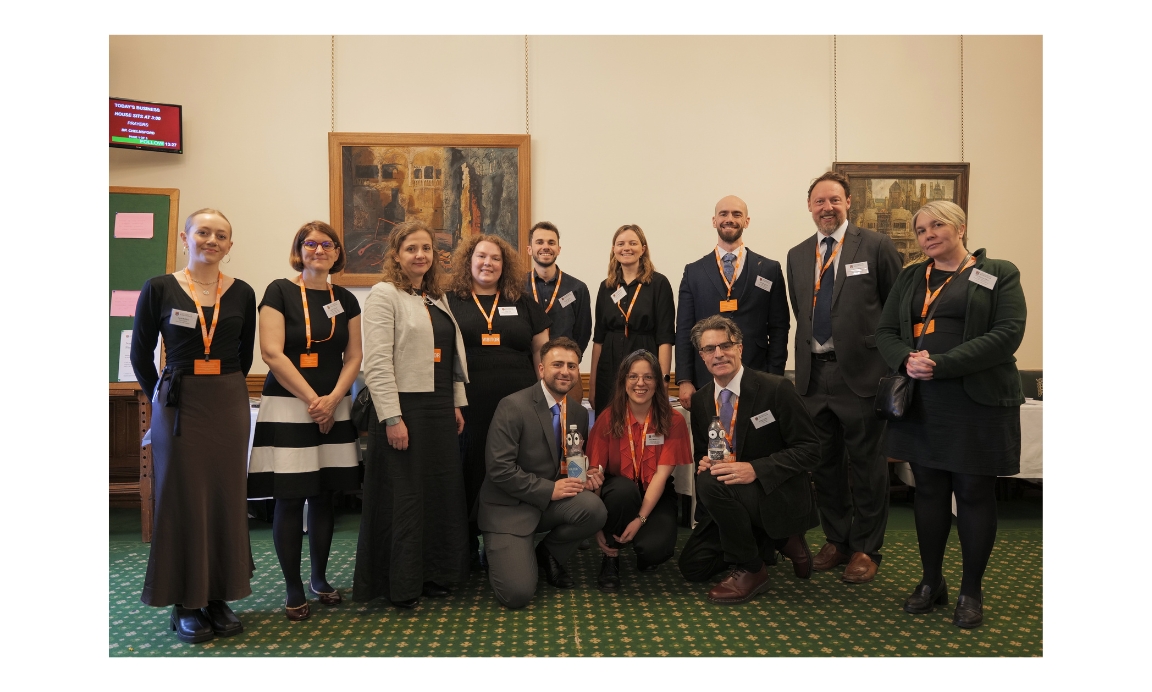 A group of smartly dressed people pose for a photo in the parliamentary reception room.