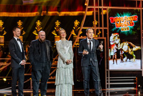 A group of people receiving an award on stage next to a poster advertising the animatronic dinosaurs of Dinosaur World Live