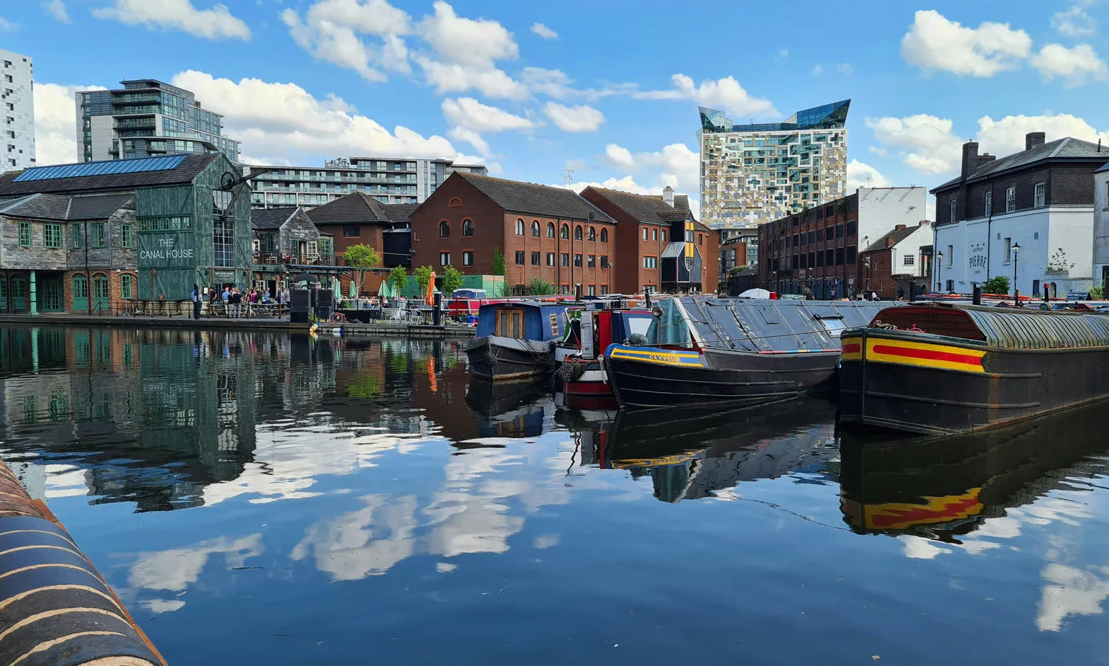 Moored narrow boats at Birmingham's Gas Street Basin, with the sky and clouds reflected in the water
