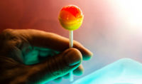 A hand holding a red and yellow lollipop