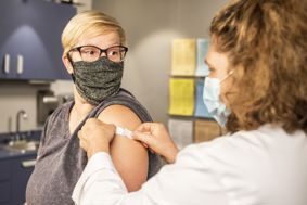 A masked female doctor putting a plaster on a masked woman who has had a vaccination