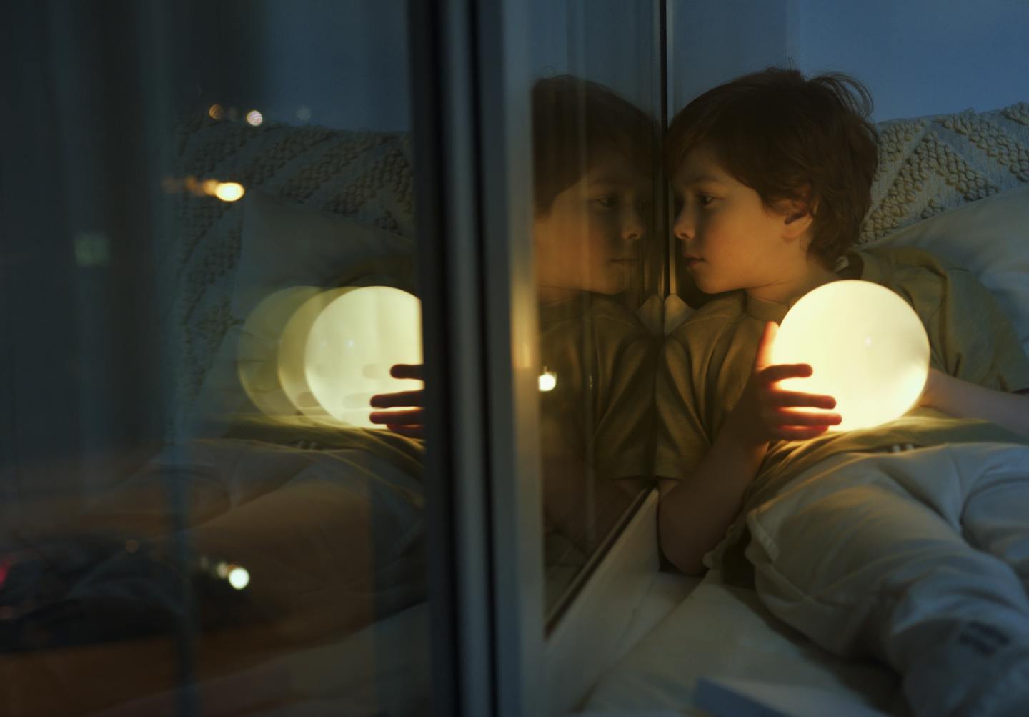 Child awake looking out of window holding night light