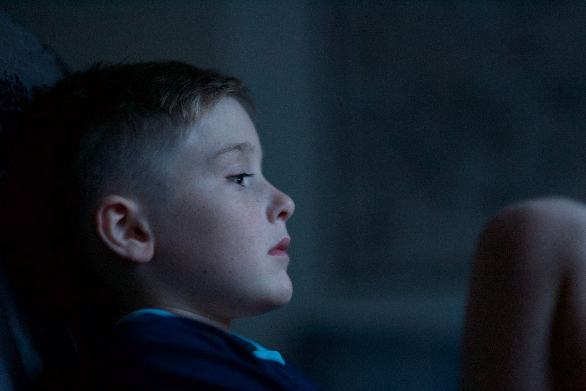 A melancholy young boy staring off into space in a darkened room
