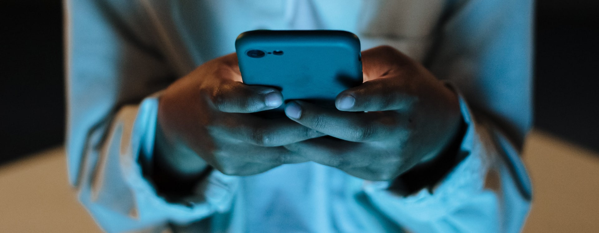 A young person's hands holding and using a smartphone in low light