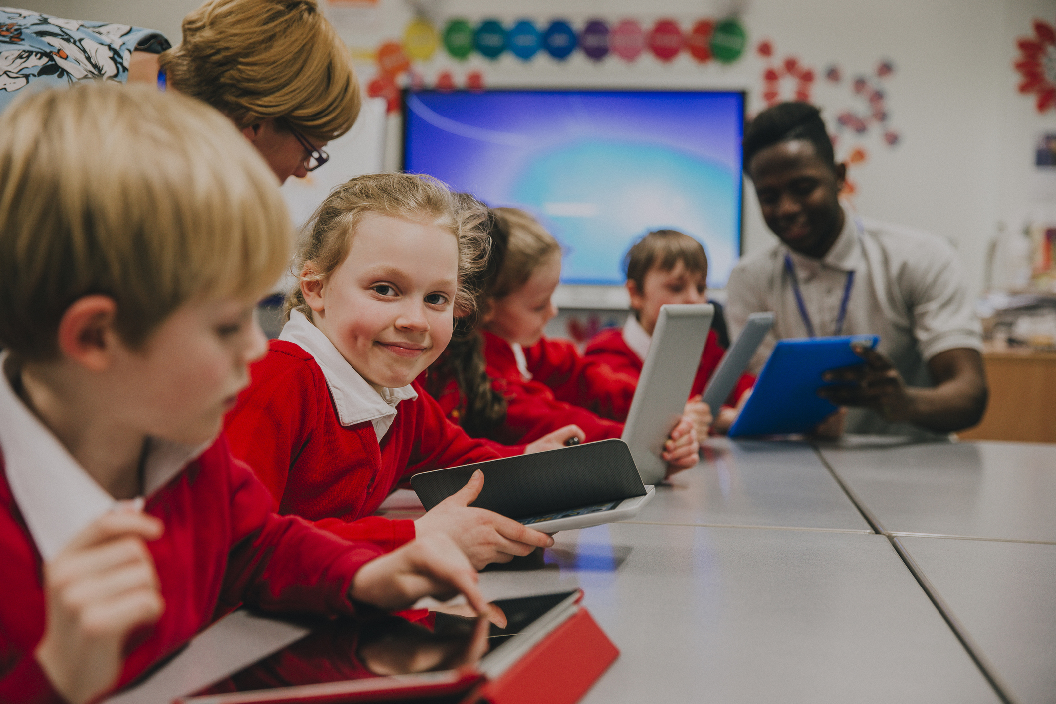 Primary school children using tablets with help from two teachers