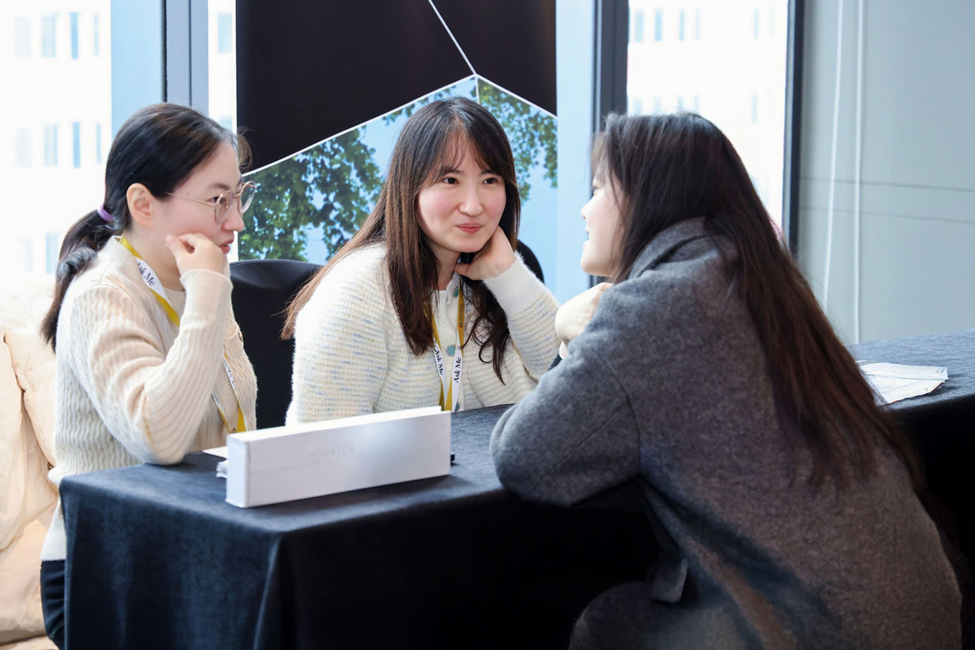 Three young Chinese women chatting to each other over a desk