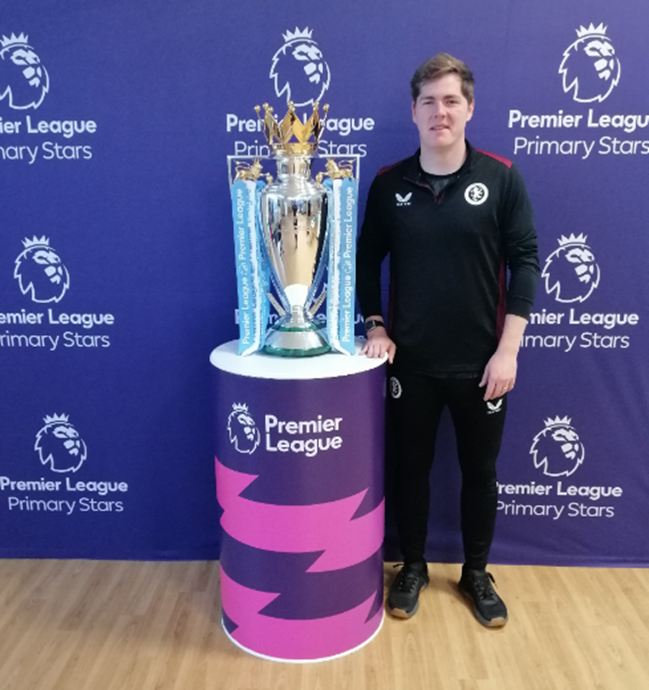 A male standing next to a premier league trophy