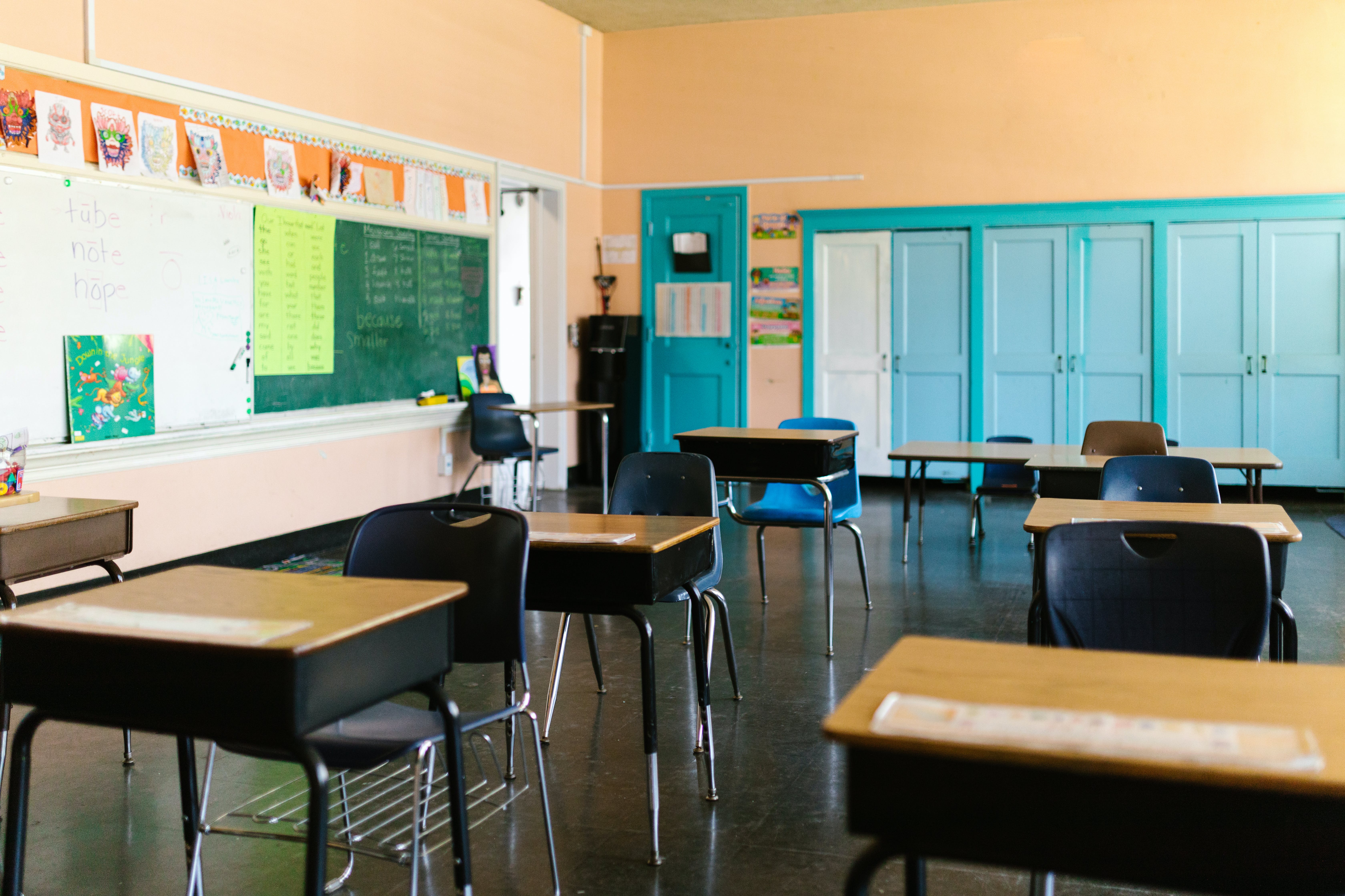 An empty classroom with desks and blue storage cupboards in the background