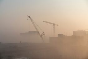 Silhouettes of cranes and partially constructed buildings through dusty sky