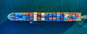 Brightly coloured shipping containers on a long boat, shot from above in the sea