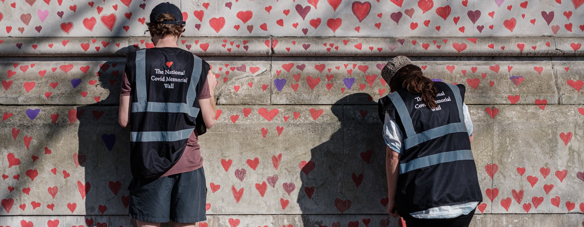 Two volunteers draw hearts onto the National Covid Memorial Wall