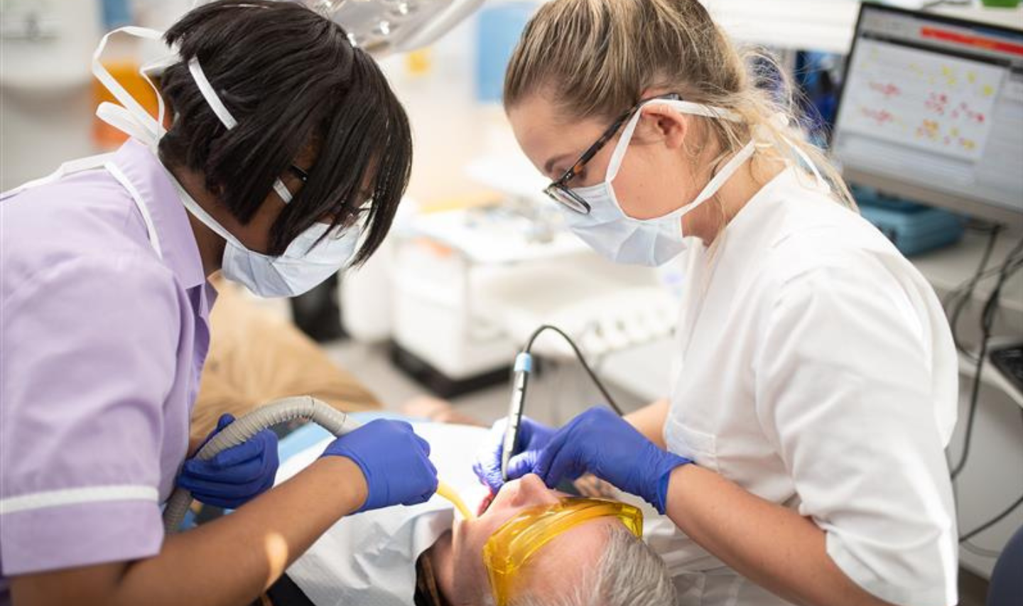 Two female dental practitioners treat a male patient