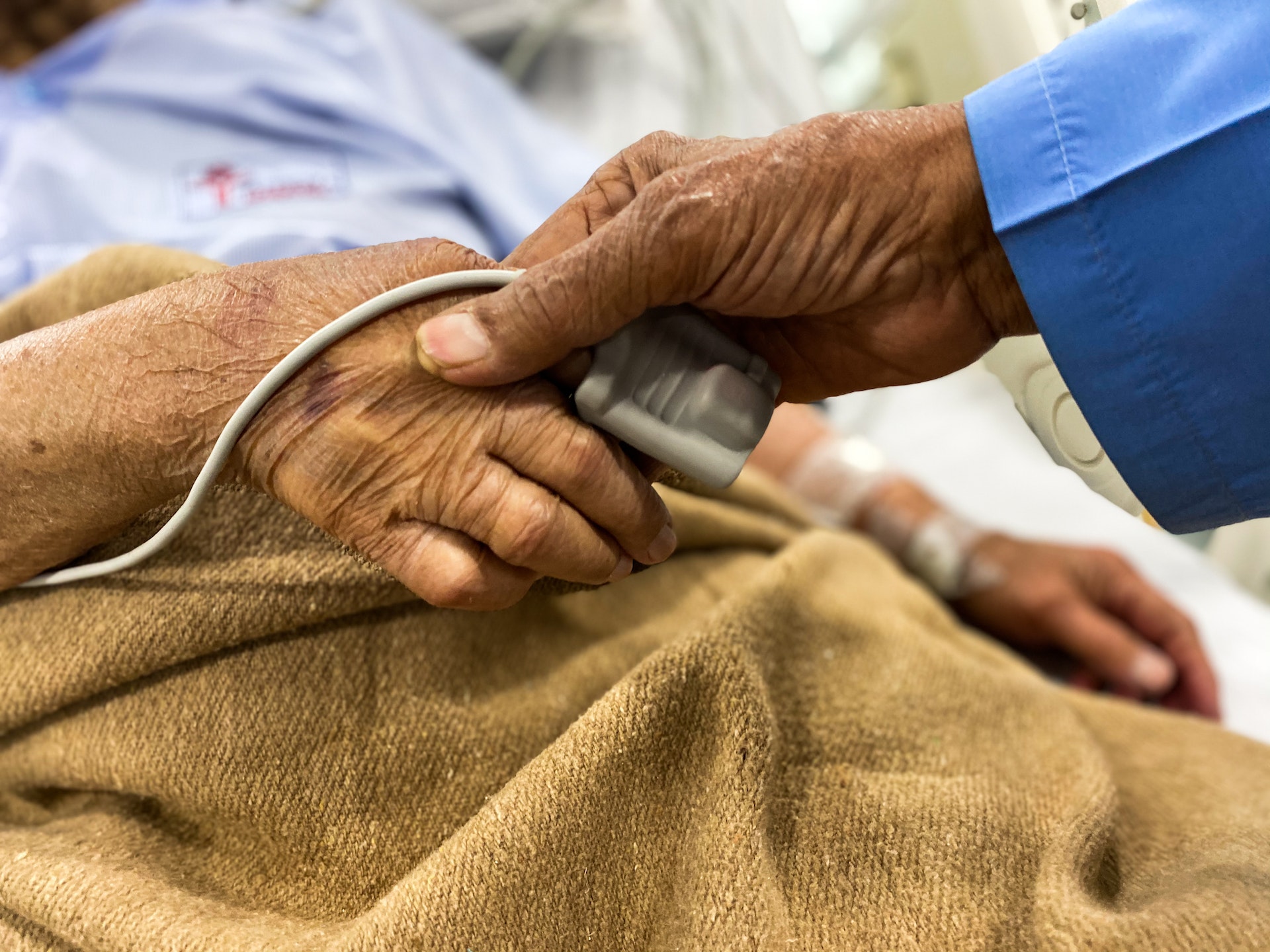 The hand of a healthcare professional holding hand of an elderly patient with a pulse checker on finger