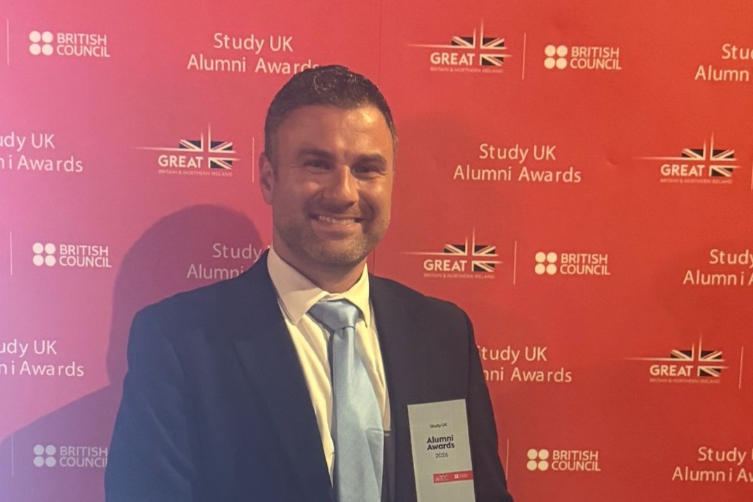 A smiling man in a suit holds an award