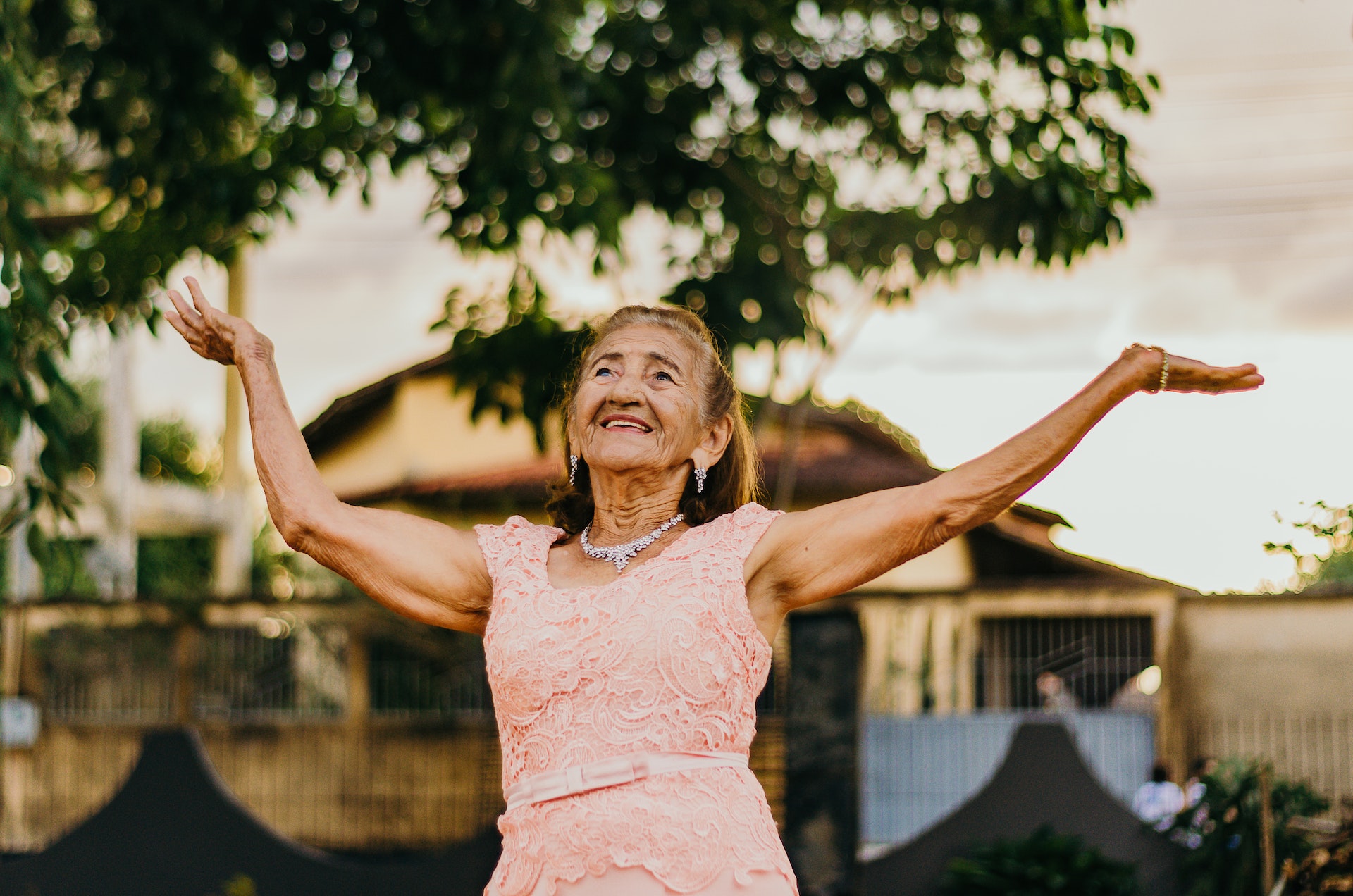 Older lady wearing formal dress dancing with both hands held up in the air