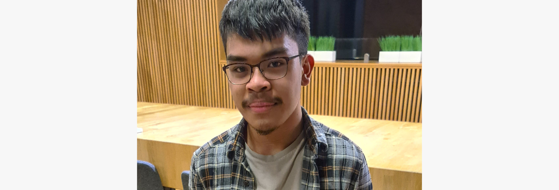 Jhundon, a male student with short black hair and glasses, smiles at the camera while sat in a lecture theatre